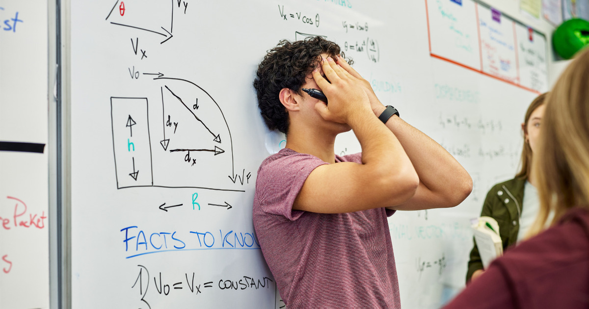 Male student standing with hand over his face and his back to a whiteboard with trigonometry problems